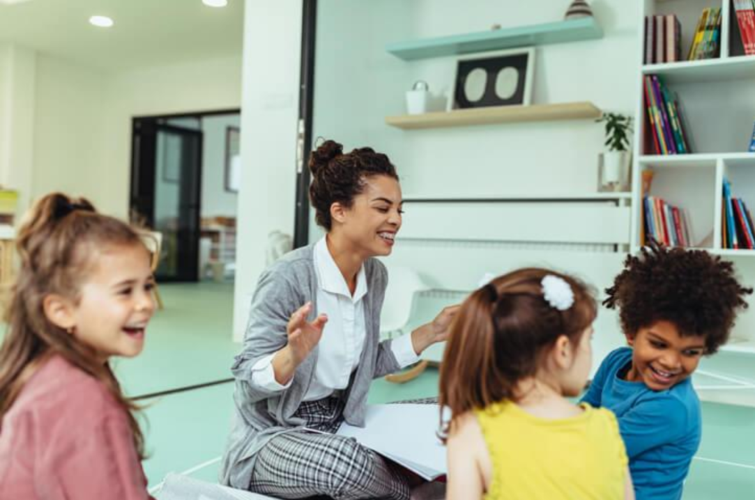 Early childhood educator leading a group activity with young children in a bright childcare classroom.