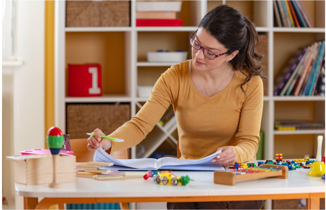 Early childhood educator reviewing observations and planning activities at a table with learning materials.