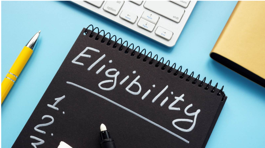 Notebook displaying an eligibility checklist beside a computer keyboard and office supplies.