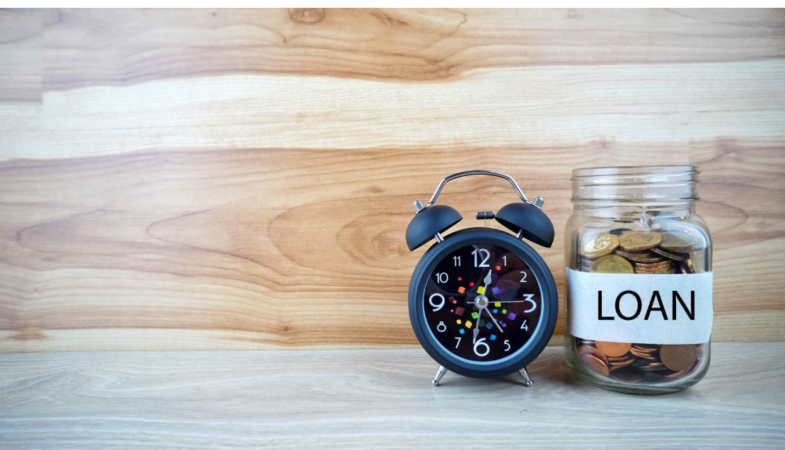 Alarm clock beside a jar of coins labelled “Loan,” representing student-loan repayment deadlines.