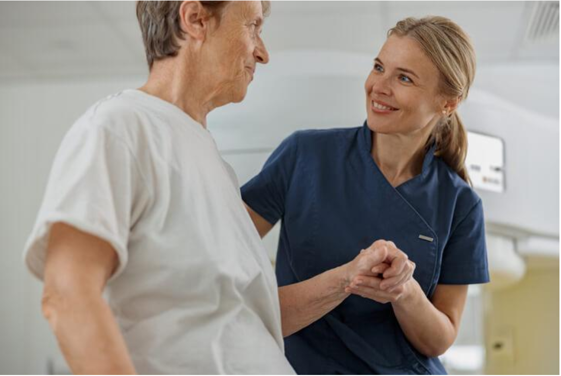 Continuing Care Assistant supporting an older adult with mobility while offering reassurance and compassionate care.