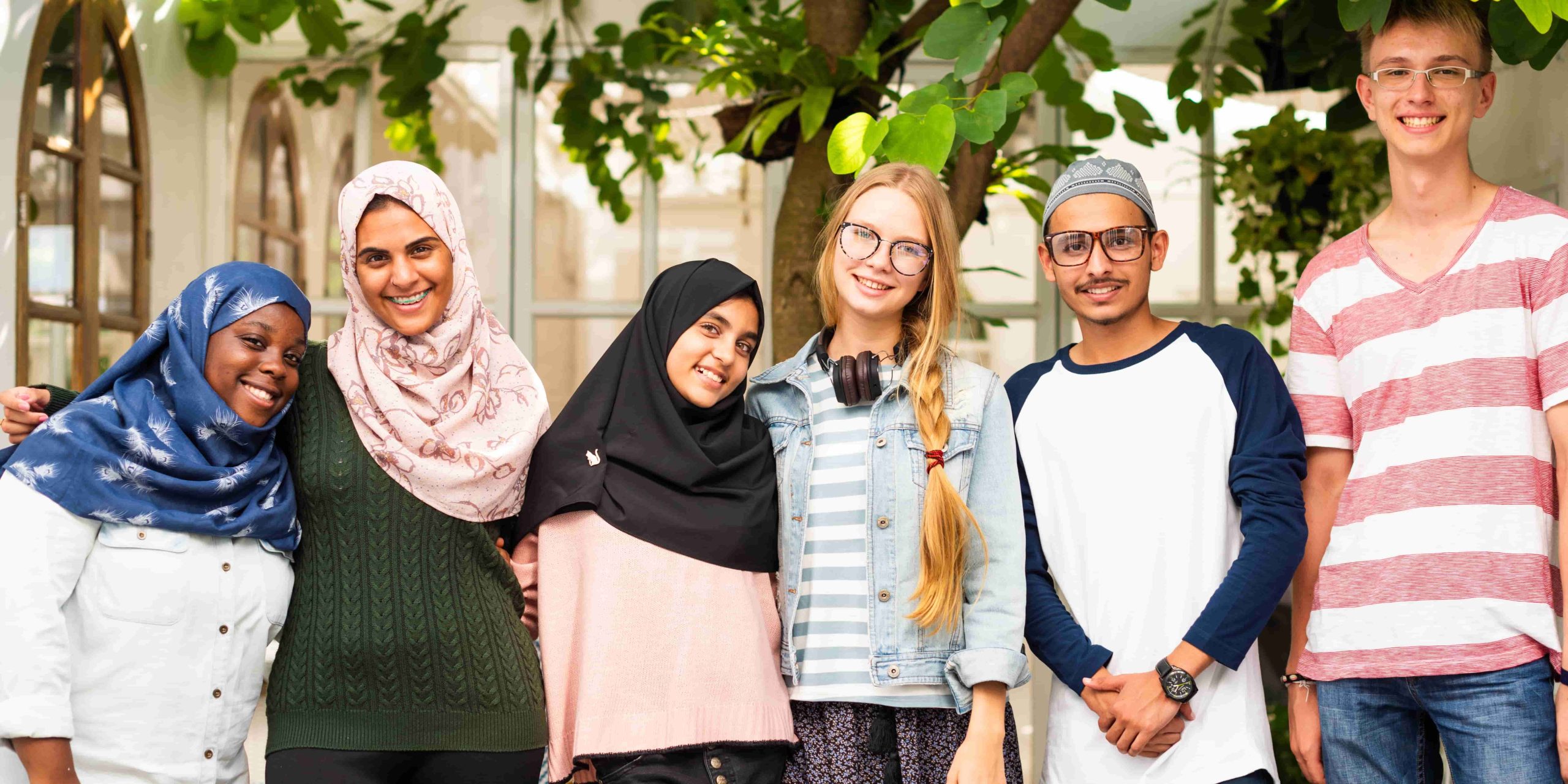 Group of diverse young adults smiling outdoors. Friends of various ethnicities enjoying time together. Happy, diverse, and friendly group portrait. Diverse young adult group in front of a house.