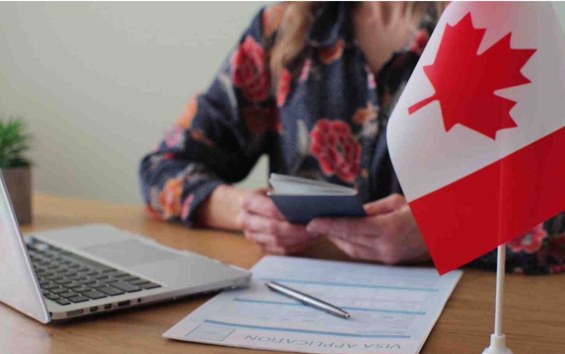 International student holding a passport beside a Canadian flag, laptop, and visa application form, representing study permits, co-op placements, internships, and practicum opportunities in Canada.