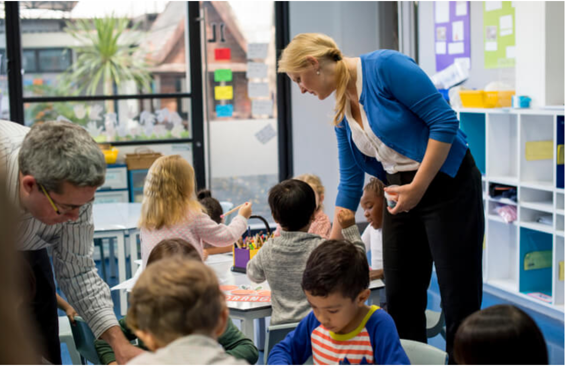 Early childhood educator guiding children through colourful art and play-based learning activities on the classroom floor.