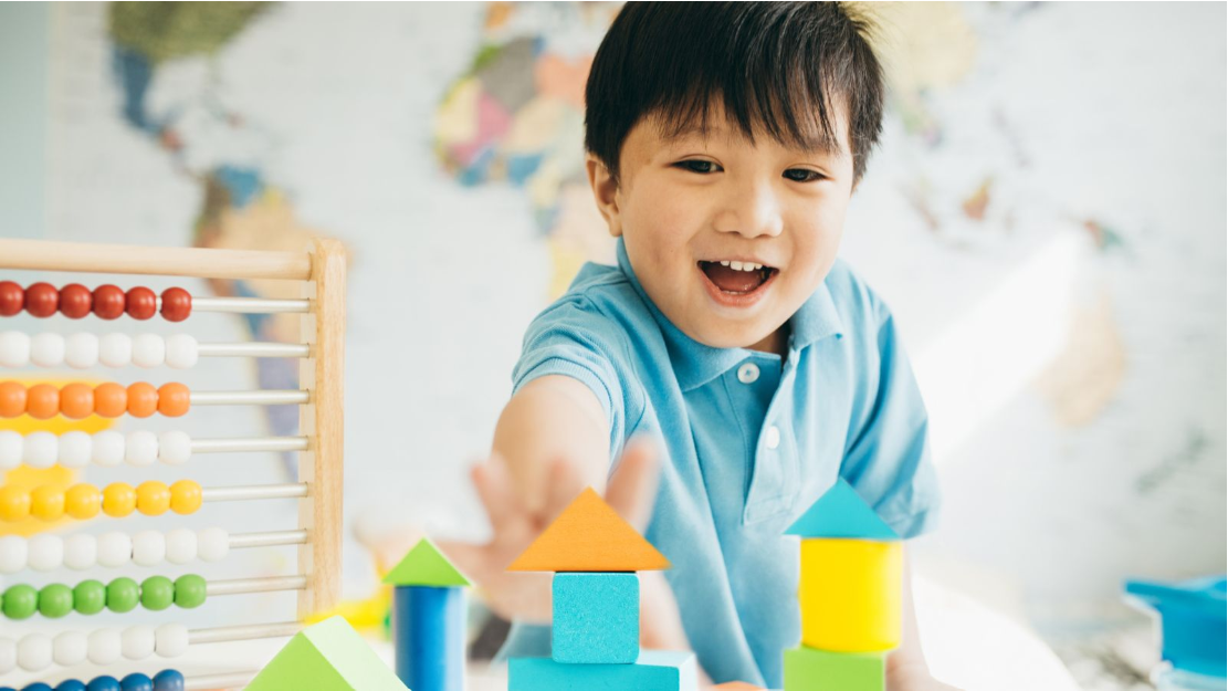 Young child building colourful block structures beside an abacus during an early learning activity.