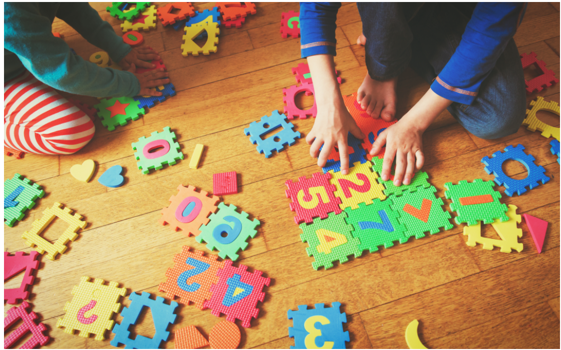 Children using colourful number, letter, and shape puzzle pieces during a play-based early learning activity.