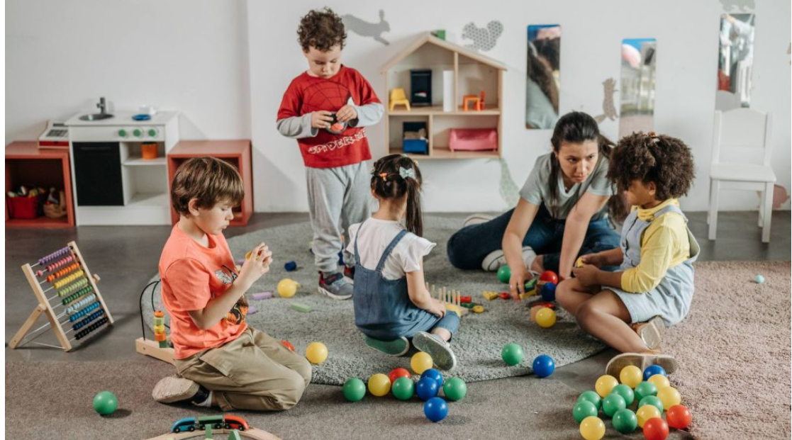 Early childhood educator guiding a diverse group of children during a play activity in a childcare classroom.