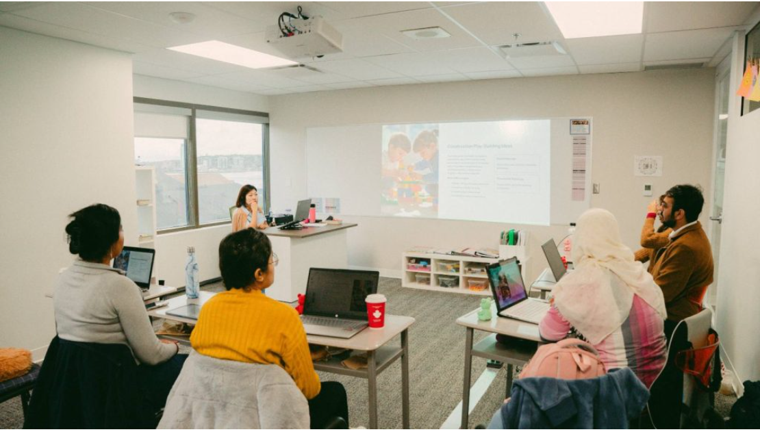 Adult students attending an Early Childhood Education class with laptops and course materials.