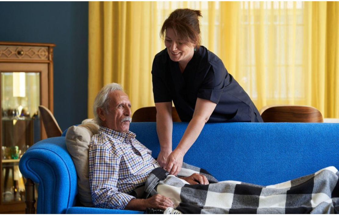 Care assistant supporting an older adult at home, showing compassionate daily care as the human foundation of healthcare