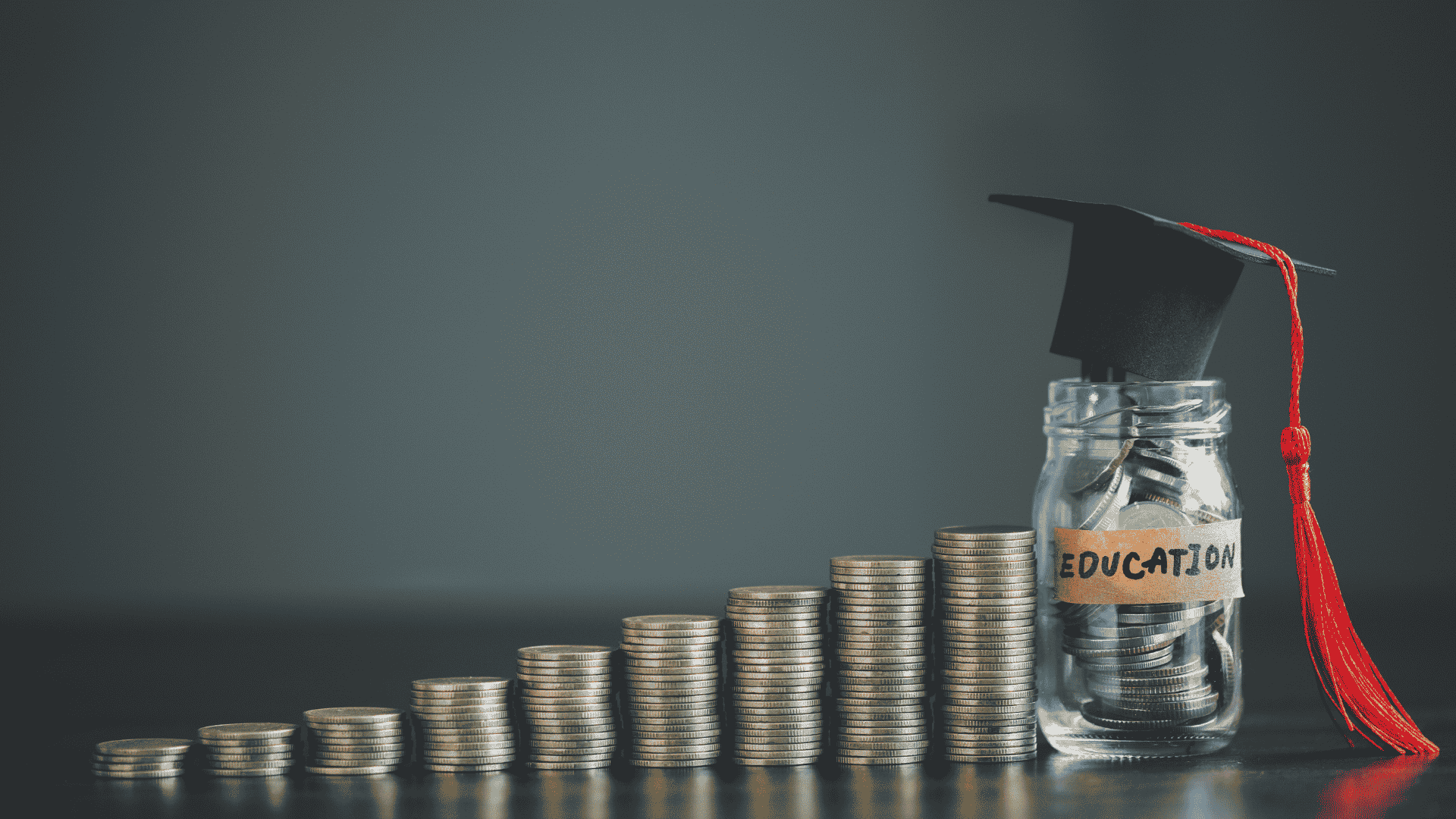 Stacks of coins increase in height next to a glass jar labeled "EDUCATION" filled with coins and topped with a graduation cap.